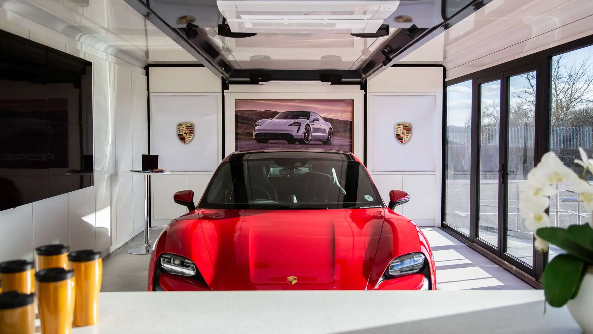 Red Porsche Taycan displayed inside Pulse Drop Deck hospitality trailer with Porsche branding showroom lighting and panoramic glazing