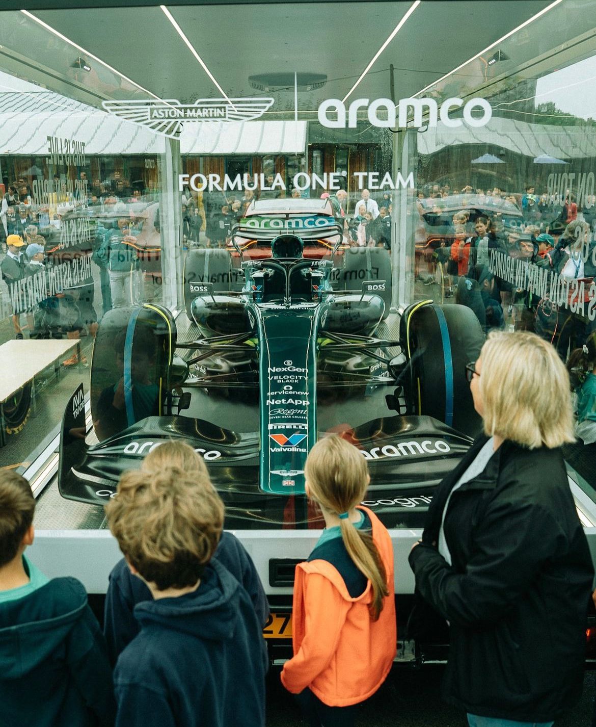 Children at UK school visit watching Aston Martin Aramco F1 car inside The Clear Idea Transparent Showcase Trailer during nationwide UK tour