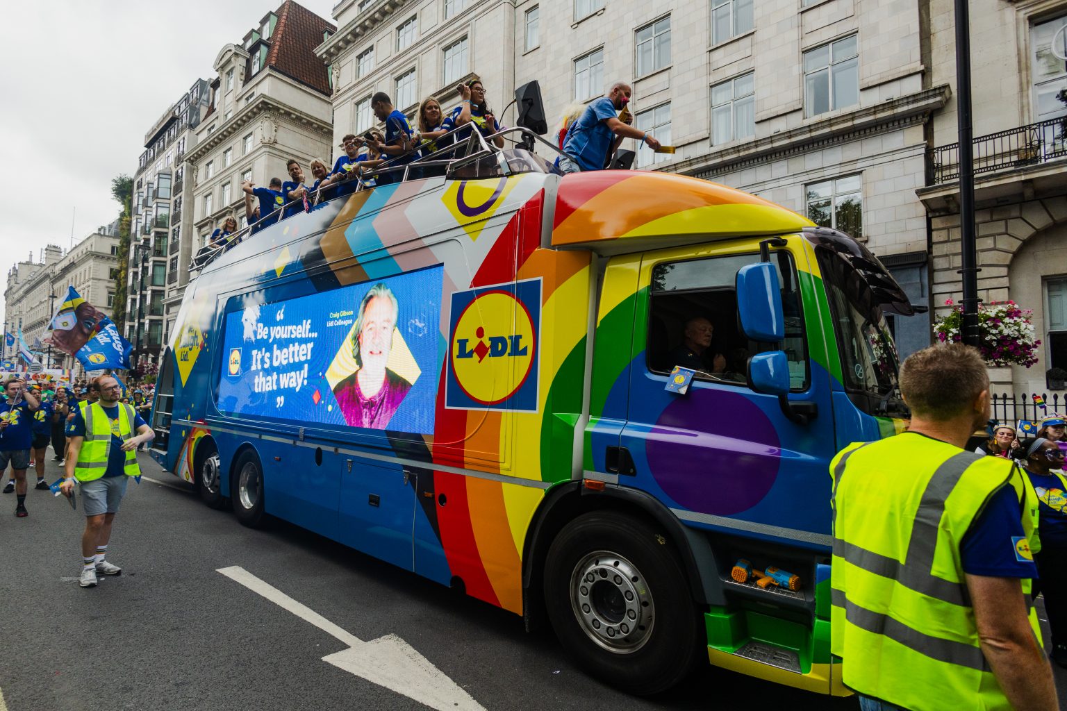 LED ShowTruck exhibition truck side profile at London Pride parade with Lidl branding rainbow graphics and performers on upper deck
