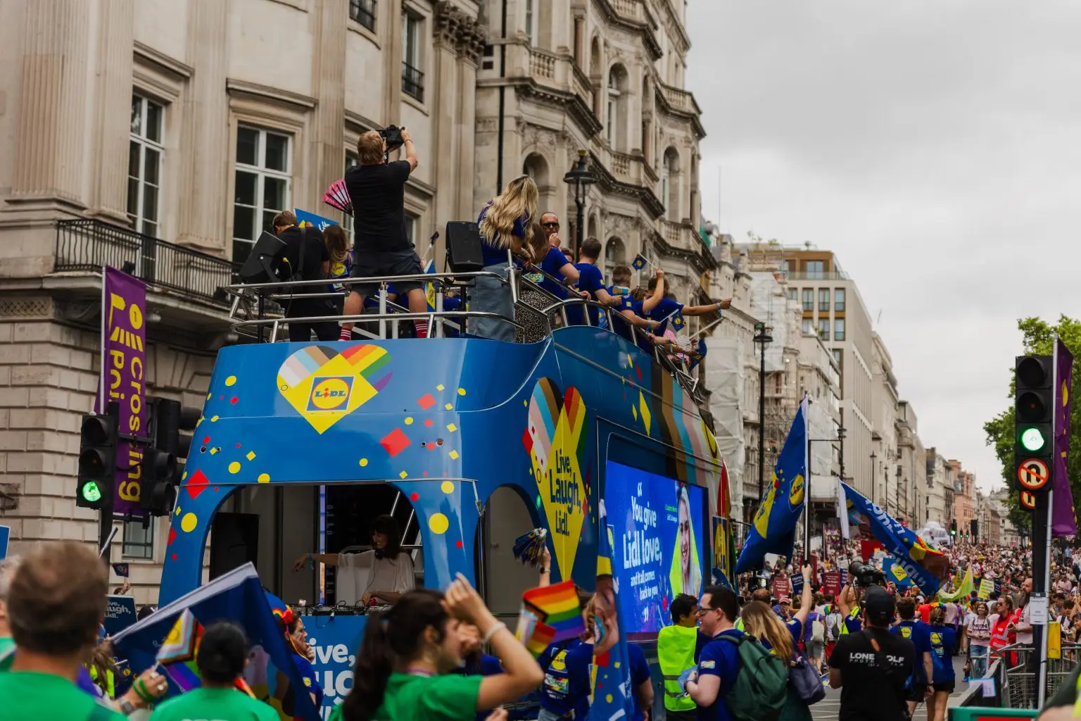 LED ShowTruck exhibition truck wide shot at London Pride parade with Lidl branding performers celebrating on upper deck and crowds lining the route