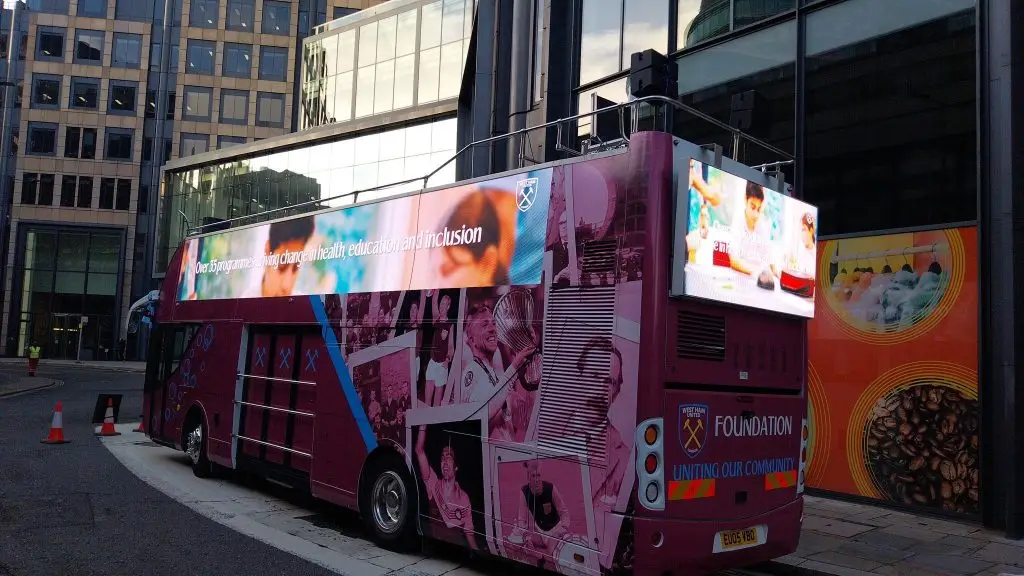 LED HyperBus promotional bus back profile in City of London with West Ham Foundation wrap and LED screen displaying social value content