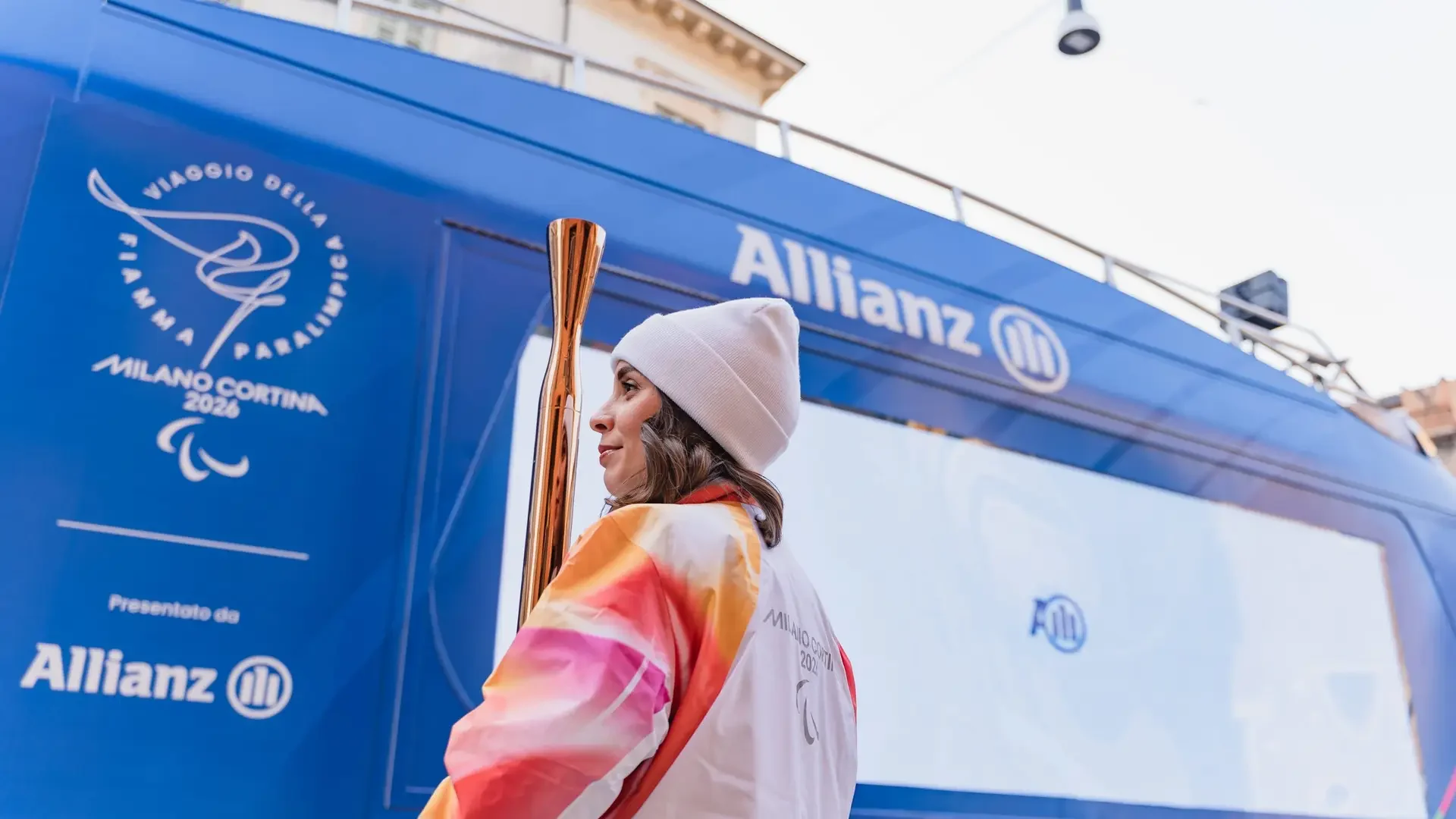 Torchbearer beside the Allianz ShowTruck during the Milano Cortina 2026 Paralympic Torch Relay